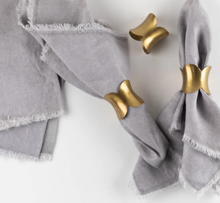 Gold scallop napkin rings on grey napkins on white table.