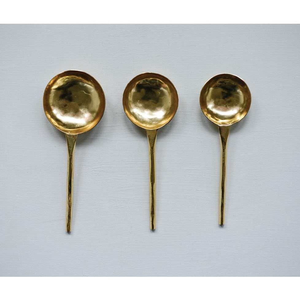 set of three hammered gold serving scoops on light blue background 