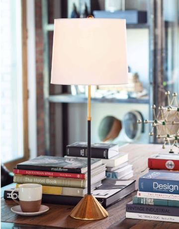 Black and gold lamp with white lamp shade on desk with books.