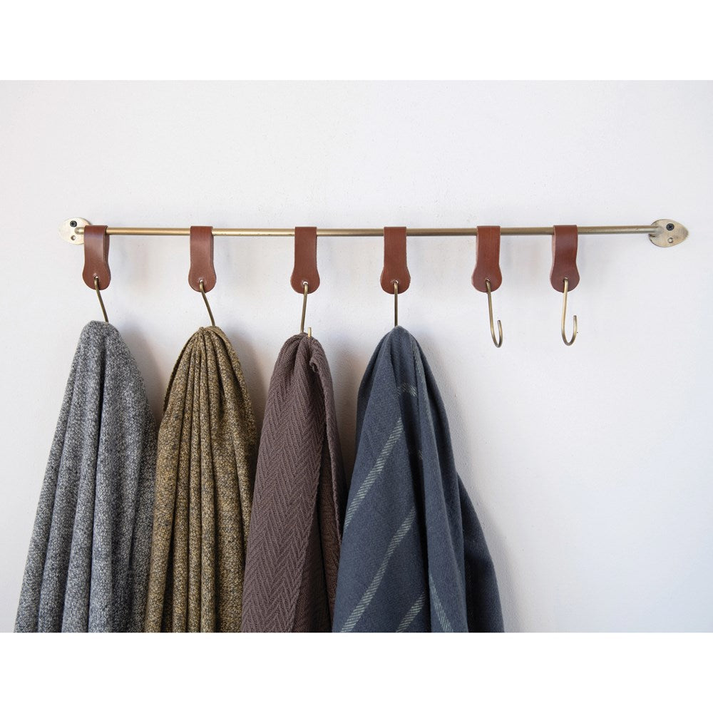 brass rod with leather hooks on white background showing throws draped on hooks