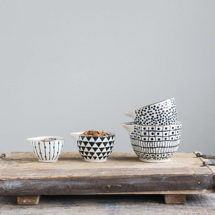 Black and white stoneware measuring cups with gold rim stacked inside each other on on wood board with pale background